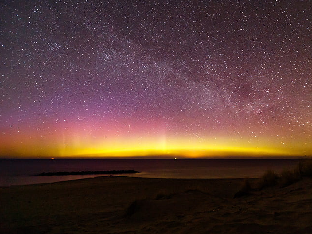 Image of the night sky with stars above and a big, yellow glow along the horizon